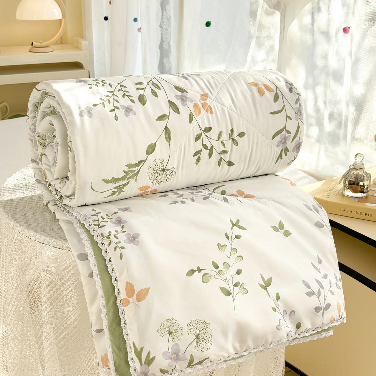 White comforter with a green and purple floral print and lace trim folded on a table.