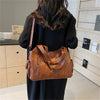 A woman is holding a brown vintage leather tote bag with multiple pockets against a light wood background.