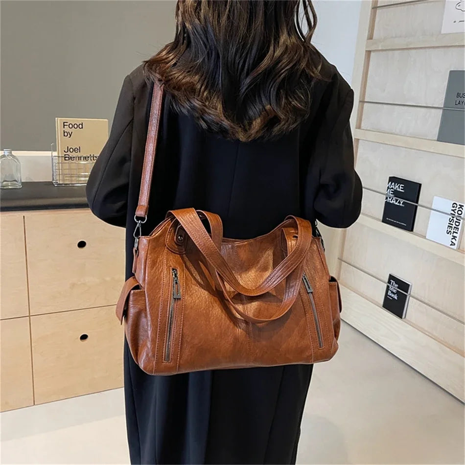 A woman is holding a brown vintage leather tote bag with multiple pockets against a light wood background.