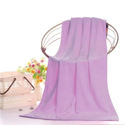 A purple ultra-soft microfiber bath towel hanging on a wooden hanger with a floral background.