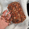A hand holds a ball of hand-dyed variegated yarn with shades of brown and orange on a white textured fabric.