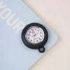 A black analog watch with a white face and red hands is pinned onto a light blue card.