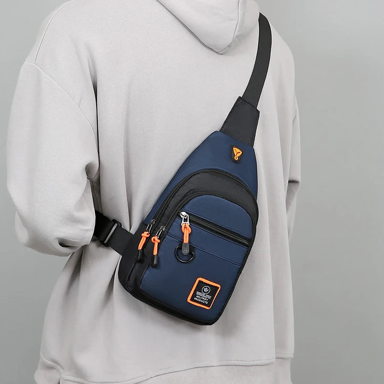 A navy blue water-resistant crossbody bag with an orange strap is shown attached to a light gray hoodie.