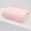 A rolled pink plush coral velvet bath towel with soft texture resting on a white surface.