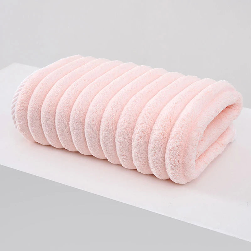 A rolled pink plush coral velvet bath towel with soft texture resting on a white surface.