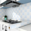 A modern kitchen featuring a white tiled splashback and a black cooktop with a stainless steel hood above.