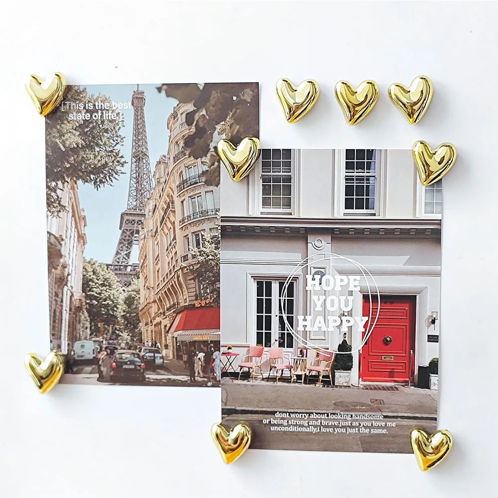 A set of twelve gold heart-shaped refrigerator magnets displayed against a background featuring the Eiffel Tower and Parisian