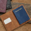 A brown leather passport holder with a navy blue passport and a white card, resting on a tan surface.