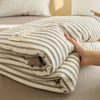 A striped breathable summer quilt with a jacquard cotton cover is folded on a bed.
