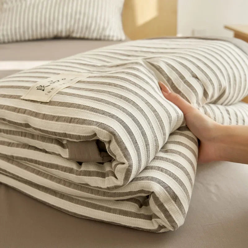 A striped breathable summer quilt with a jacquard cotton cover is folded on a bed.