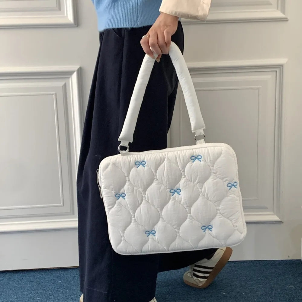 A person is holding a white quilted laptop shoulder bag with blue bows and padded protection.