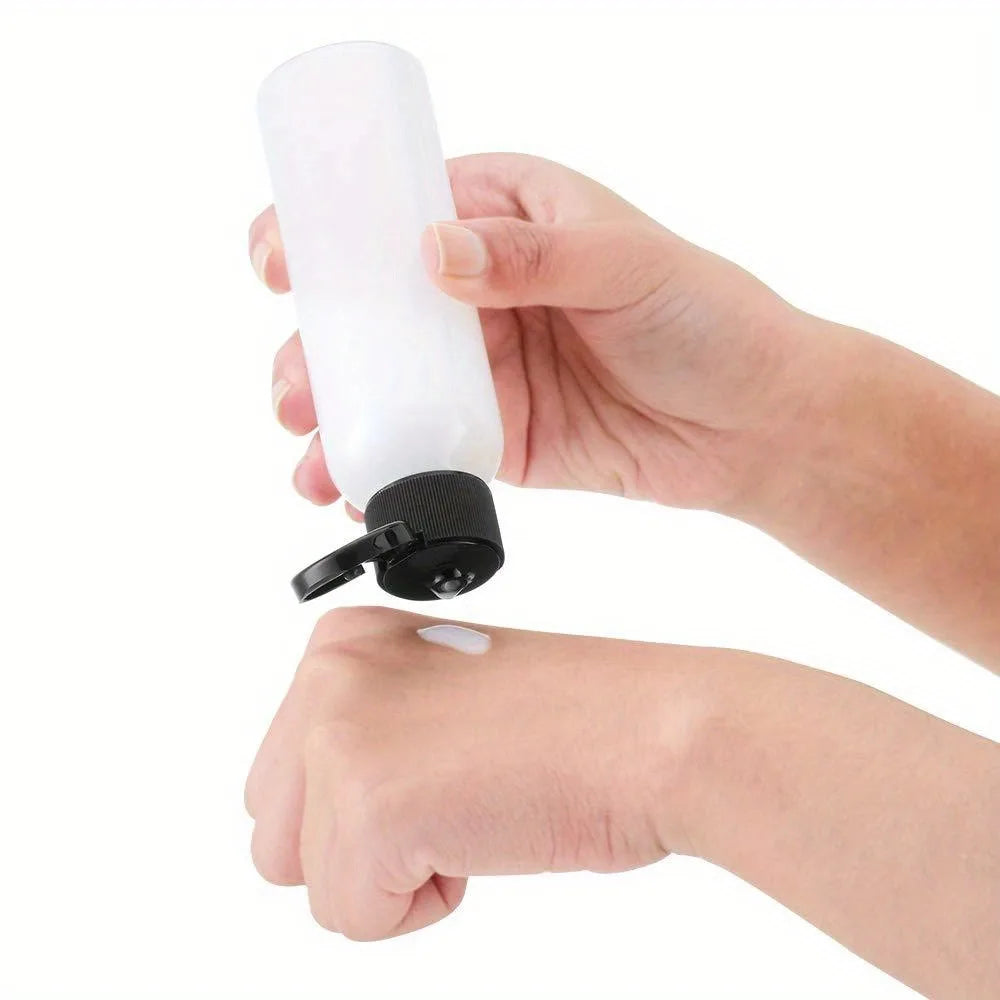 A hand is holding a white refillable travel bottle with a flip cap.