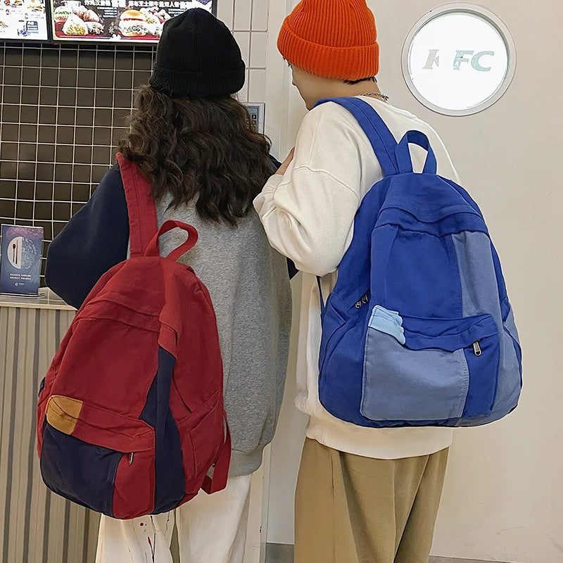 A woman wearing a white top and orange beanie is holding a blue backpack while another person wears a red backpack.