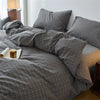 A plaid duvet cover in gray and black tones is displayed on a bed with pillows and natural light.