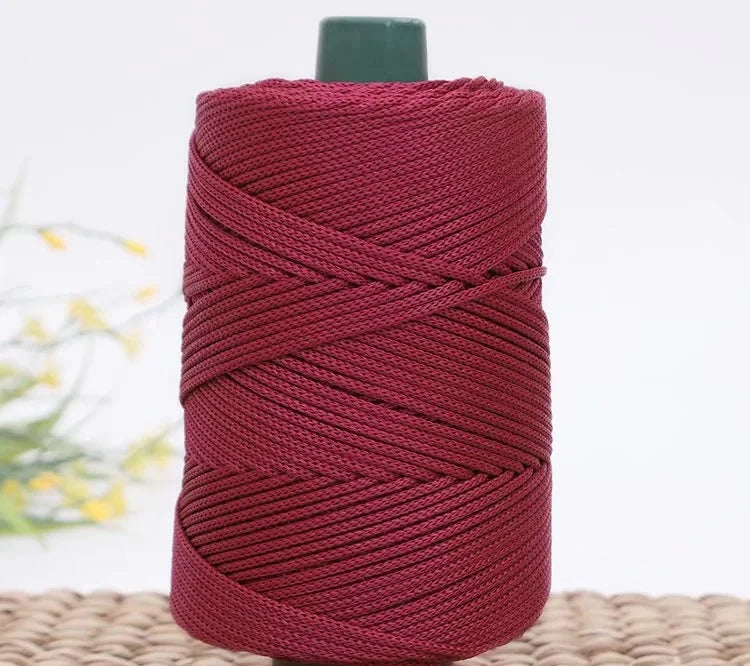 A spool of deep red crochet ice rope with a dark green cap, resting on a woven mat.