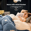 A warm milk velvet blanket is shown draped over a bed, with a person relaxing under it.