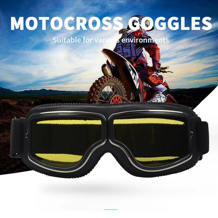 A pair of black retro foldable motocross goggles are displayed in front of a background featuring a motorcycle and outdoor te