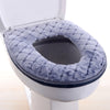 Una cubierta de asiento de inodoro impermeable gris y mullida instalada en una taza de inodoro blanca.
