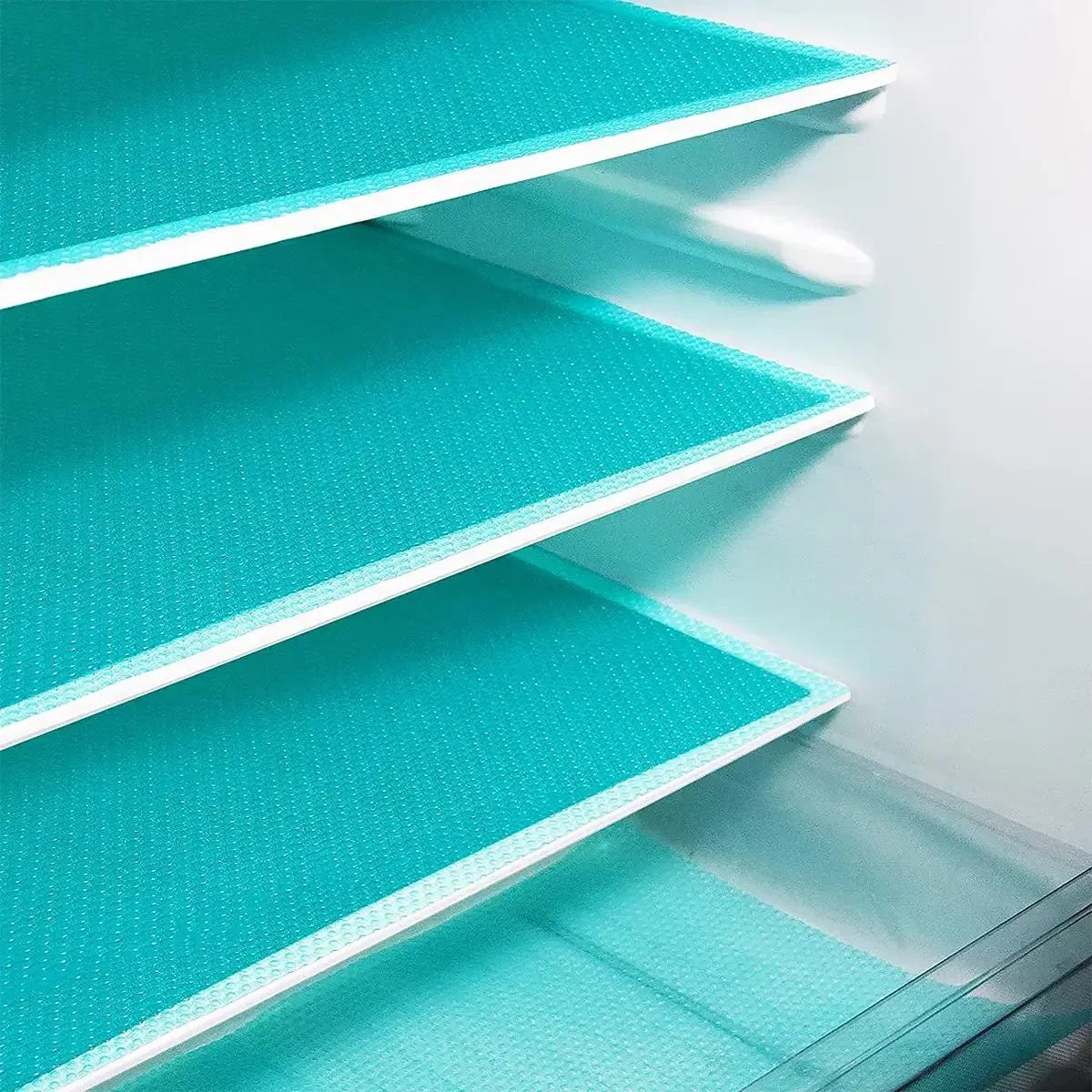 A close-up view of three stacked teal silicone shelf liners for refrigerators.
