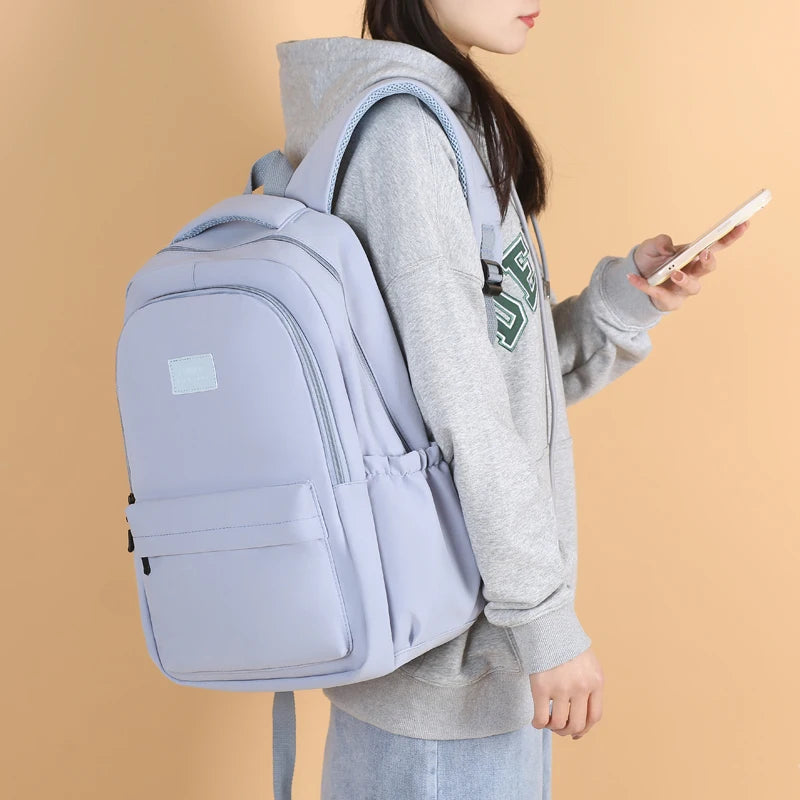 A person is holding a light purple waterproof nylon laptop backpack with gray hoodie and jeans.