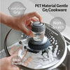 A hand is using a dark silicone press dish brush with a built-in soap dispenser to clean cookware.