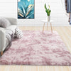 A fluffy pink velvet carpet placed in a living room with a sofa and a plant on a side table.