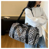 A woman holds a leopard print travel tote bag with a black strap and shoe compartment.