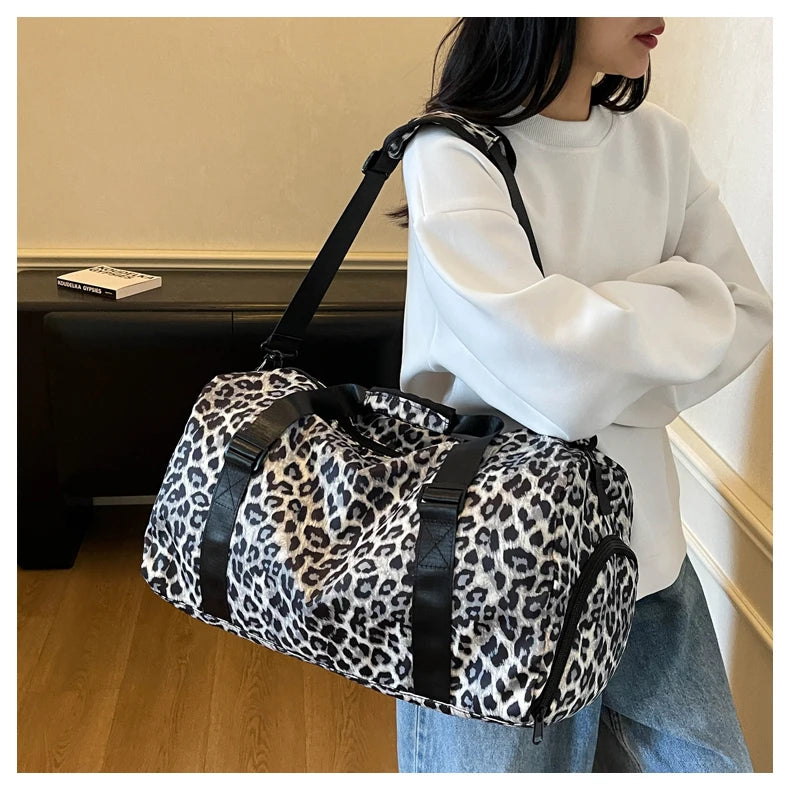 A woman holds a leopard print travel tote bag with a black strap and shoe compartment.