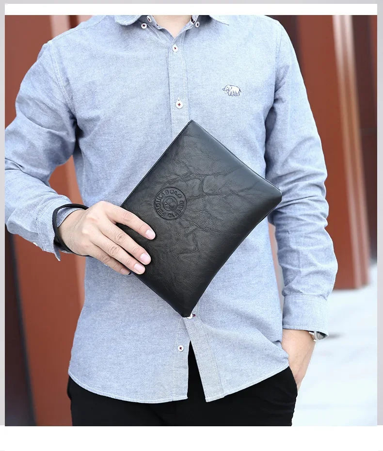 Ein Mann trägt ein hellgraues Hemd und hält eine schwarze Kunstleder-Clutch-Geldbörse.