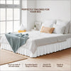 White bed with a ruffled skirt and white linens in a bright room.