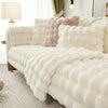 A white fluffy decorative pillow cover is displayed on a sofa, featuring soft textures and light neutral tones.