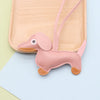A pink dachshund shaped PU leather keychain with a floppy ear and stitched details resting on a light wooden tray.