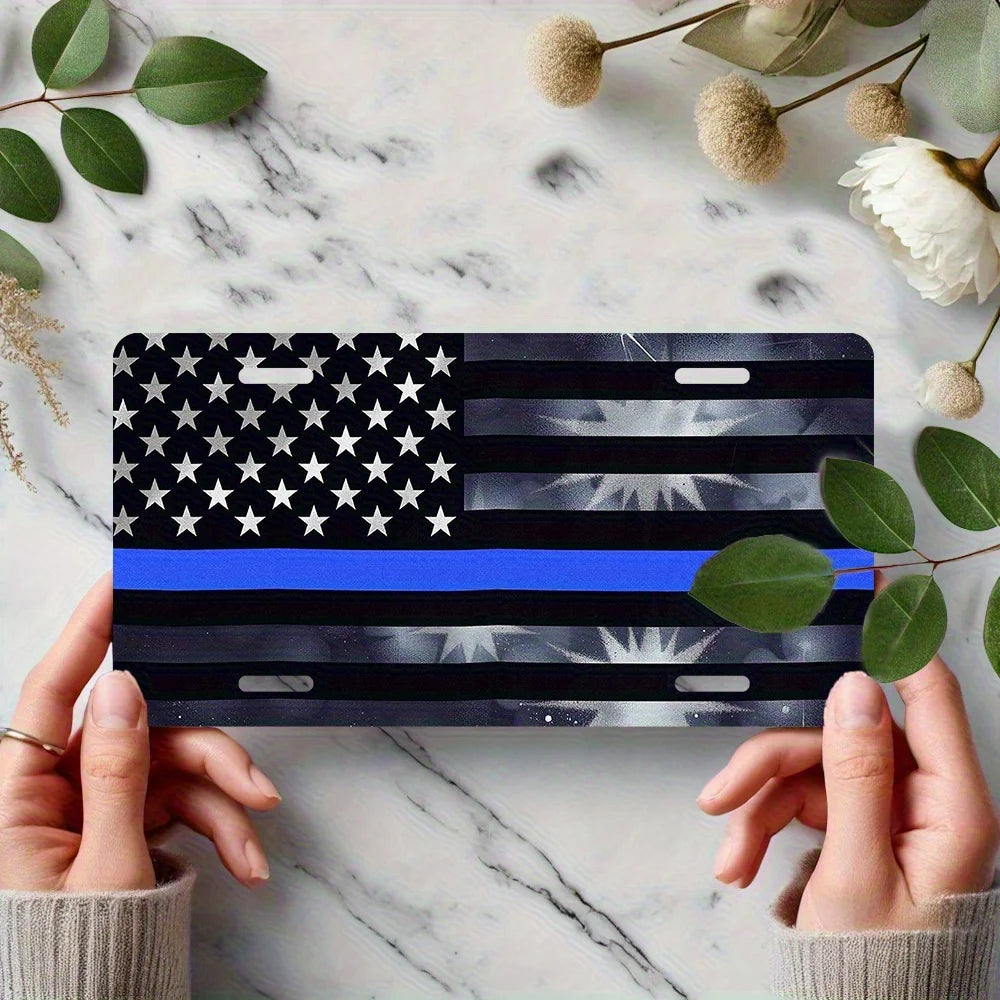 A hand holds a thin blue line American flag metal sign featuring stars and stripes on a marble surface.