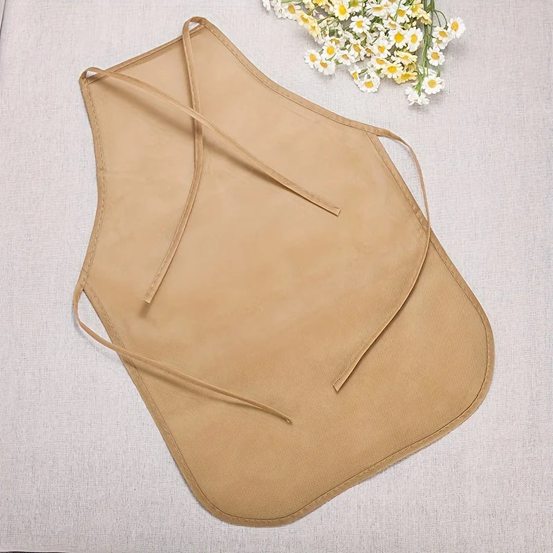 Tan non-woven fabric craft apron with tie closures lying on a light gray cloth.