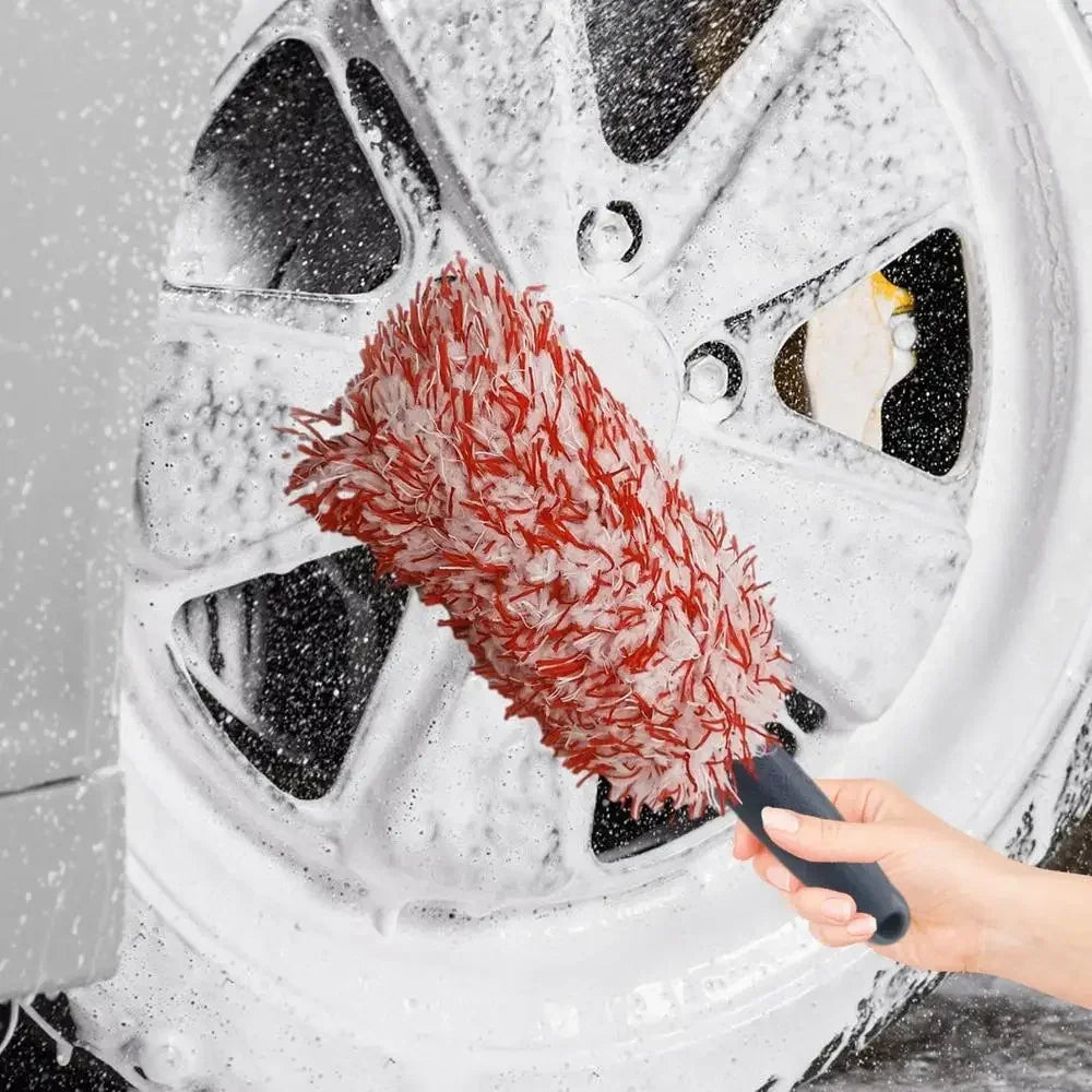 A hand is using a red plush wheel cleaning brush to clean a white car wheel.
