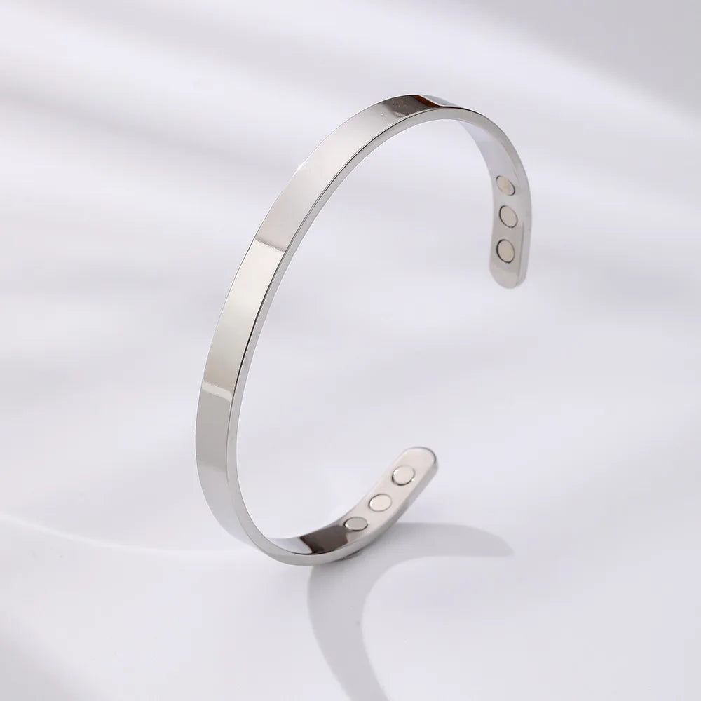 Bracelet manchette magnétique argenté réglable sur fond blanc.
