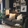A dark gray sofa in a modern living room decorated with framed art and fluffy pillows.