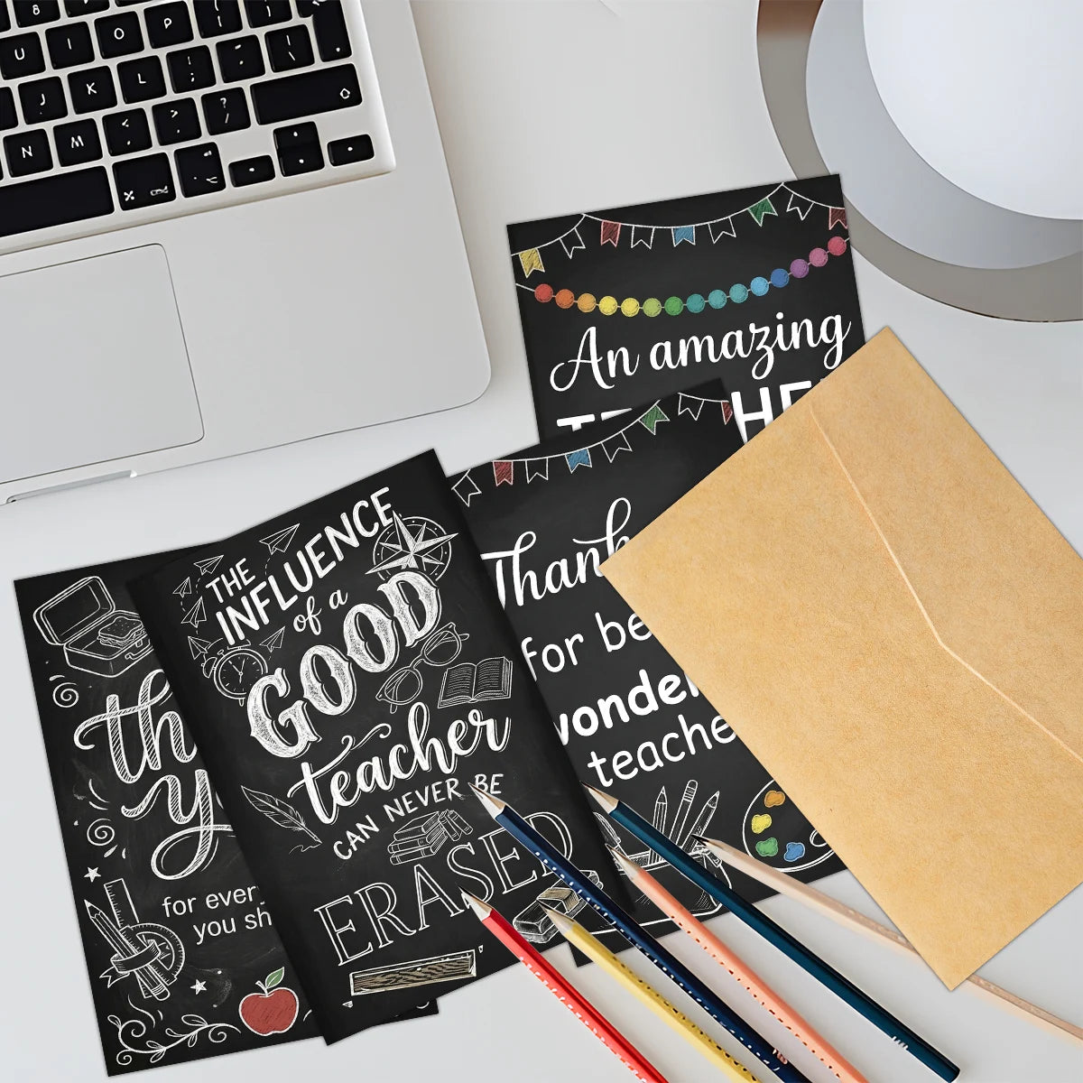 A set of six chalkboard-style teacher appreciation greeting cards and envelopes are displayed on a white desk.