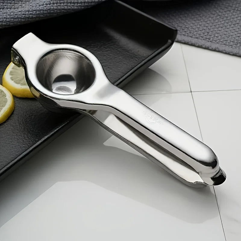 A silver stainless steel manual lemon juicer resting on a dark surface next to a lemon slice.