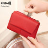 A red tri-fold wallet with a zipper and coin pocket is being held by a hand, demonstrating RFID protection.