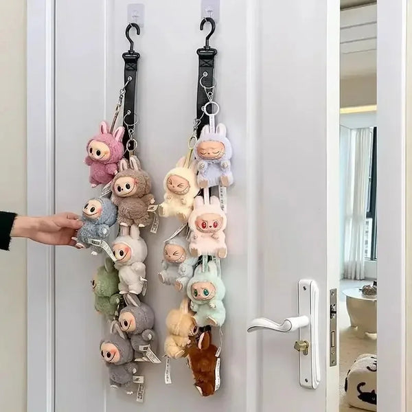 A hand is hanging a collection of soft, fluffy plush dolls from a wall-mounted display rack.