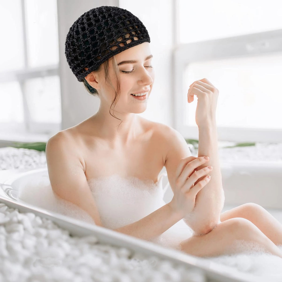 A woman wearing a black mesh crochet hair net is relaxing in a bathtub filled with foam.