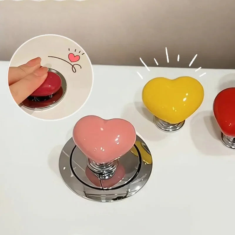 A collection of heart-shaped toilet flush buttons in pink, yellow, and red are displayed on a white surface.