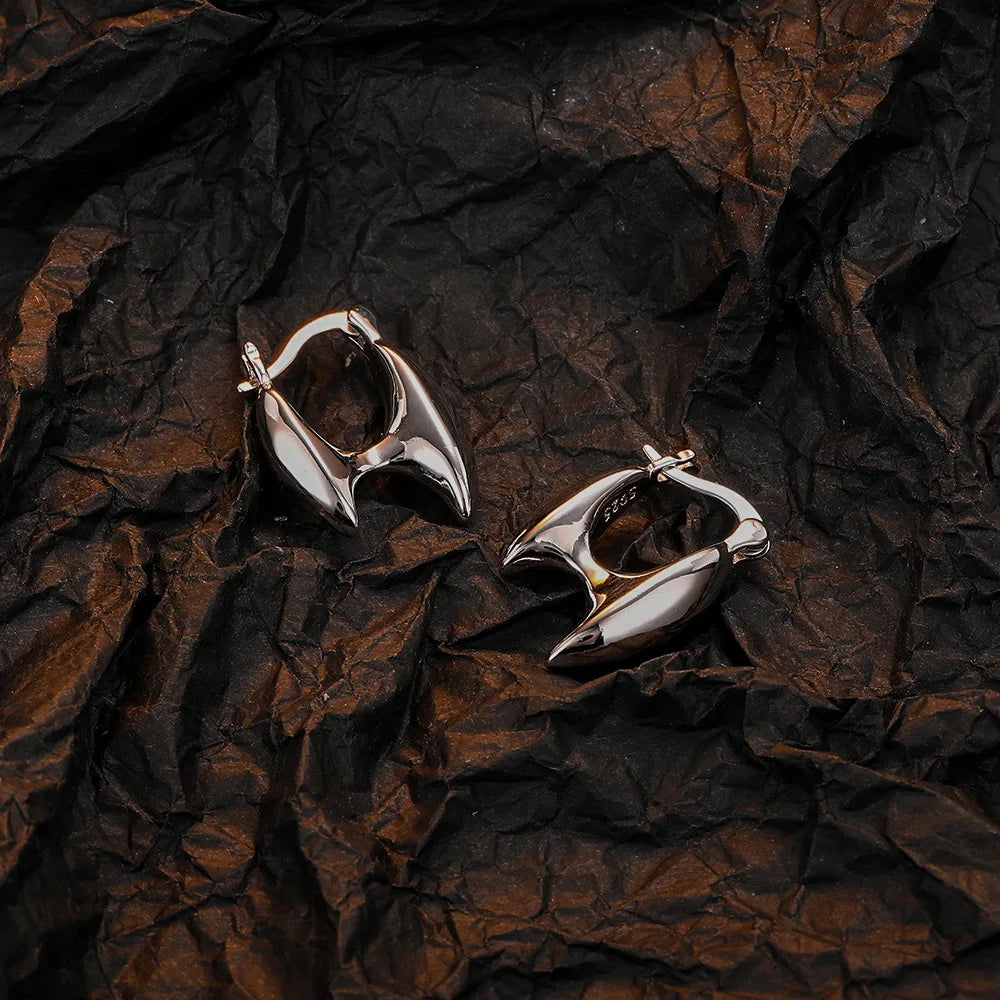 A pair of silver hoop earrings with a turquoise stone resting on dark brown crumpled paper.