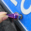A hand is holding a purple license plate screw kit, which is being inserted into a blue surface.