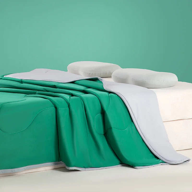 A bright green ice silk cooling blanket draped over a white surface with white pillows against a teal background.