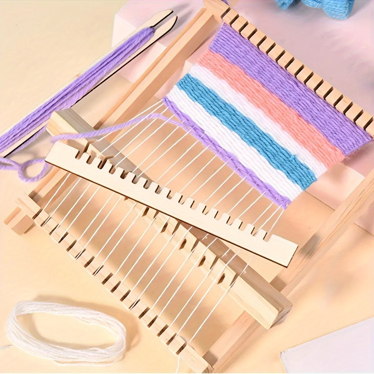 A wooden weaving loom kit with colorful striped yarn and wooden strips is shown on a light background.