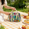 A woman holds an Insulated Picnic Lunch Bag with a cross-body strap on a checkered blanket outdoors.