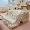 A rolled floral washed cotton gauze summer quilt in cream and pink tones resting on a pink surface.