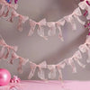 A delicate pink sheer ribbon bow knot banner garland is displayed against a light background.